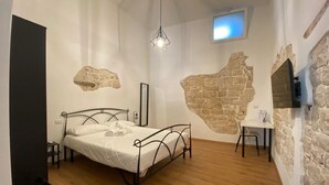A bedroom with a bed, a small table, a chair, a hanging light fixture, and a stone wall feature. - Borgo Sant' Angelo exclusive house Room 1 (Conversano)