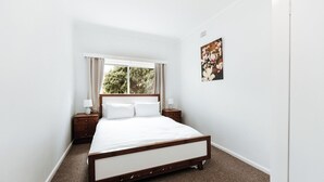 A bedroom with a large bed, a window with curtains, a nightstand, and a wall-mounted picture. - The Waratah Escape Nowra (Nowra)