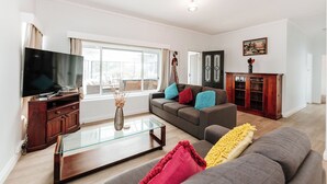 A modern living room with a flat-screen TV, a glass coffee table, a grey sofa, and a wooden cabinet. - The Waratah Escape Nowra (Nowra)