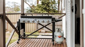 A portable grill with four burners and a propane tank on a wooden deck. - The Waratah Escape Nowra (Nowra)