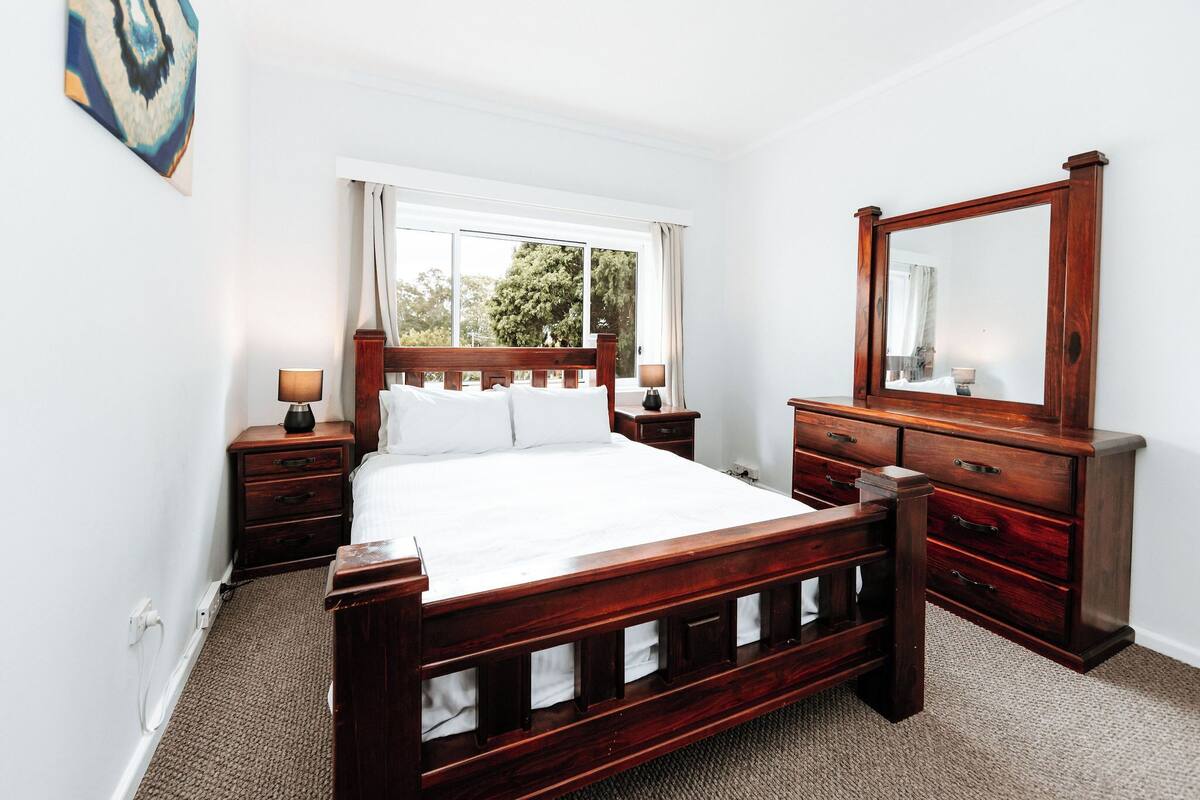 A bedroom with a wooden bed, a dresser, a mirror, and a window with curtains.