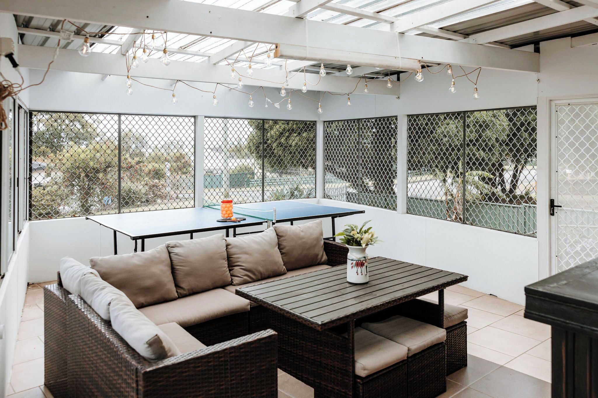 A covered outdoor seating area with a sofa, a table, and a ping pong table.