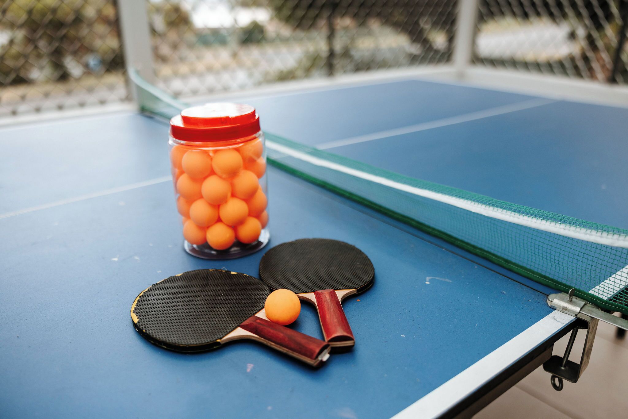 A ping pong table with two paddles and a jar of ping pong balls.