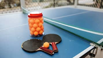 A ping pong table with two paddles and a jar of ping pong balls.