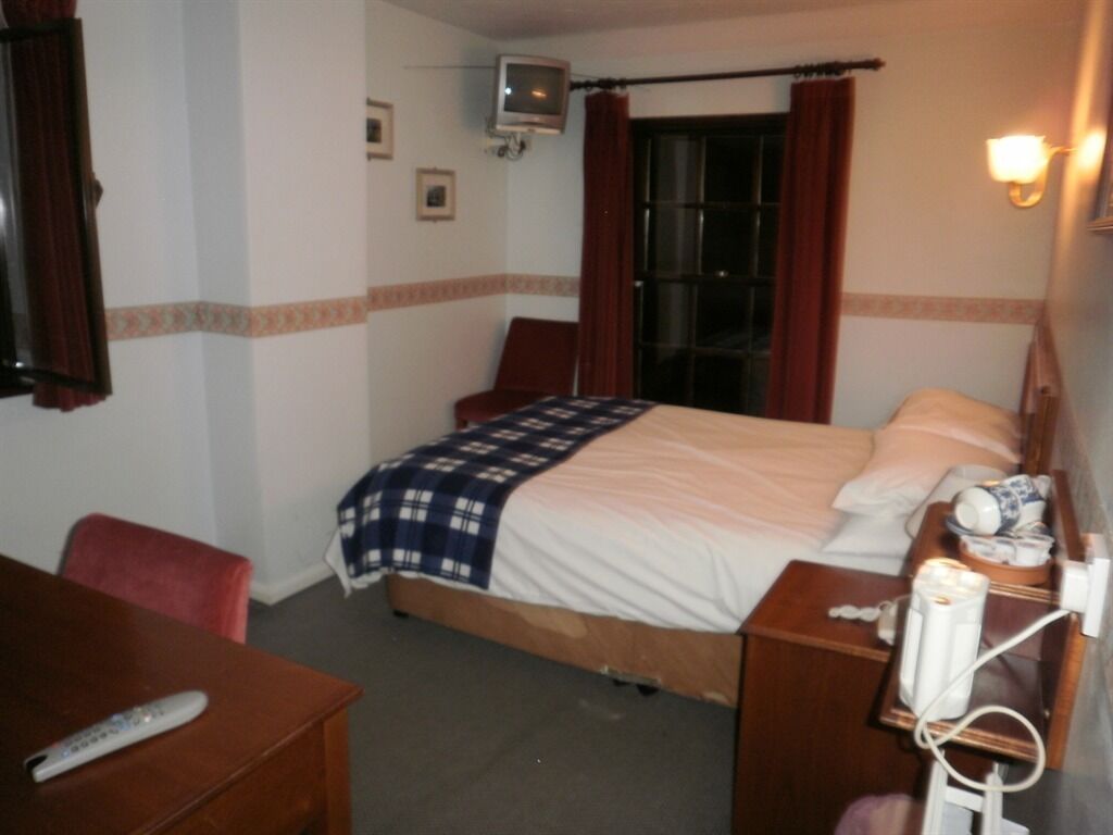 A hotel room with a bed, a bedside table, a chair, a TV, and a lamp.