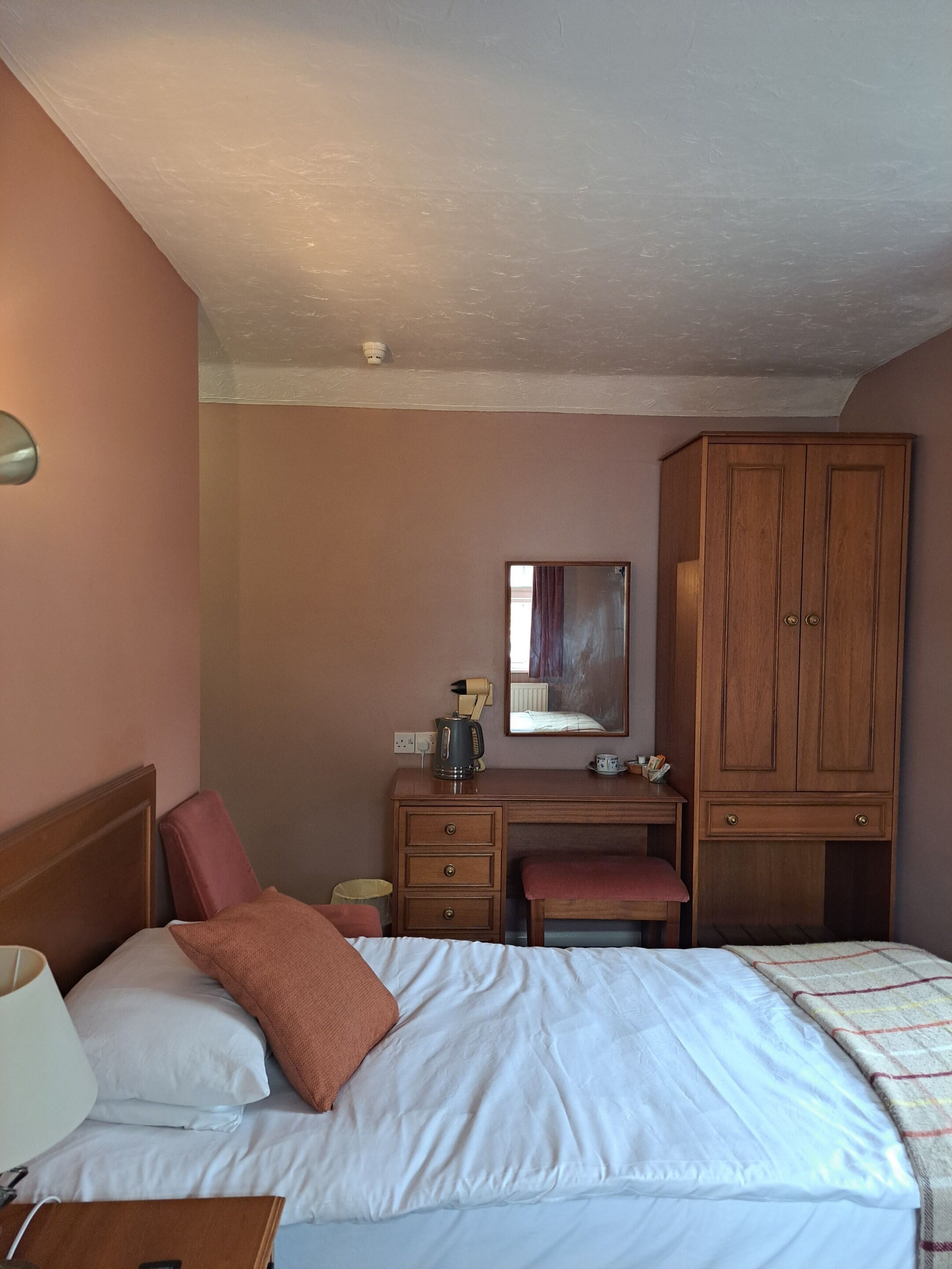 A hotel room with a bed, a desk, a wardrobe, and a mirror.