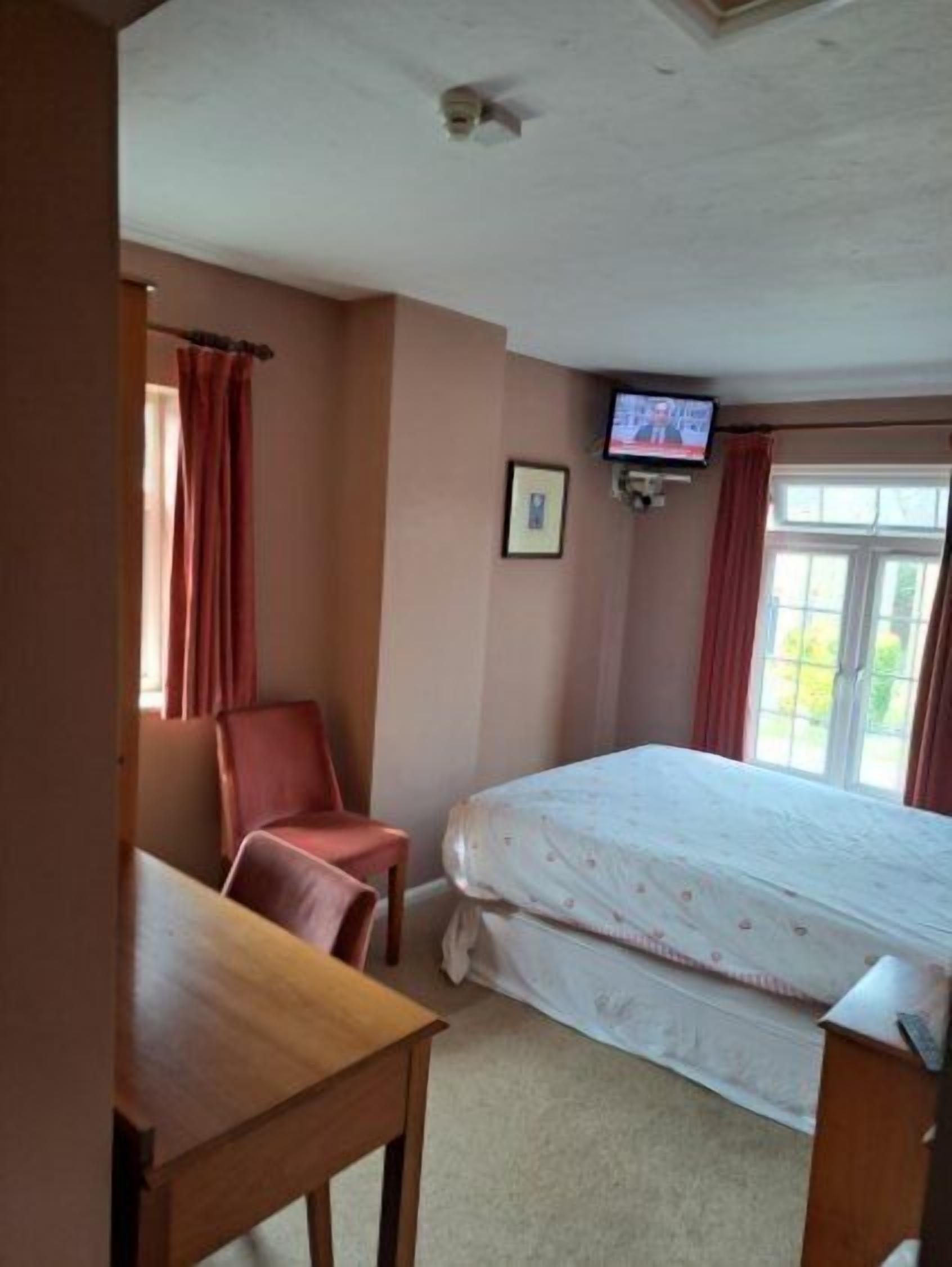 Una camera d'albergo con un letto, una sedia, una scrivania, una televisione e una finestra con tende.