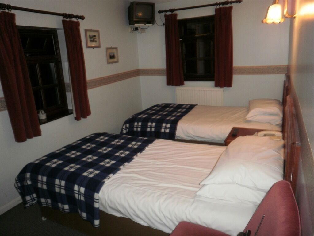 A room with two beds, each with a plaid blanket and white pillows. There is a small television on the wall and a window with curtains.