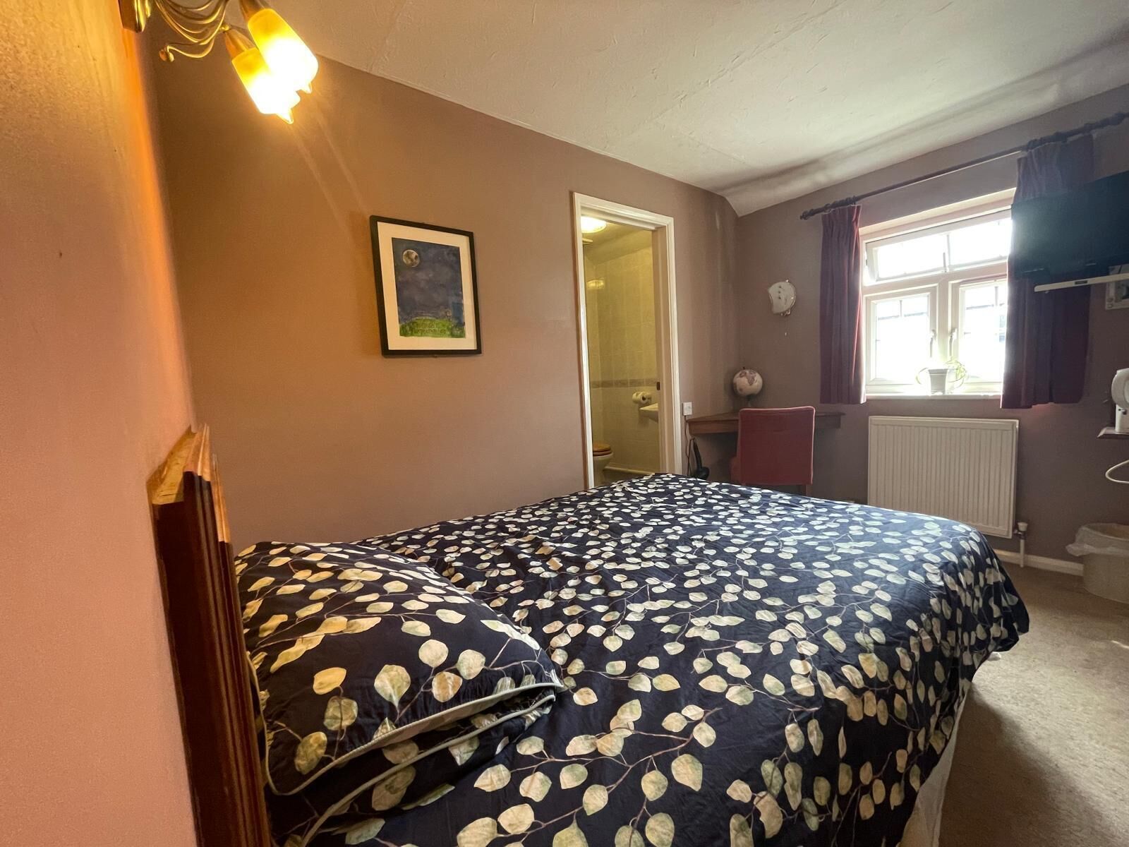 Un dormitorio con una cama, un cuadro en la pared y una ventana con cortinas.