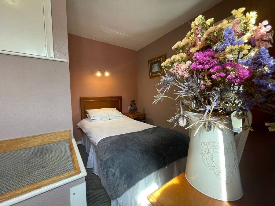 Un dormitorio con cama, una mesita de noche, un florero y un cuadro en la pared.