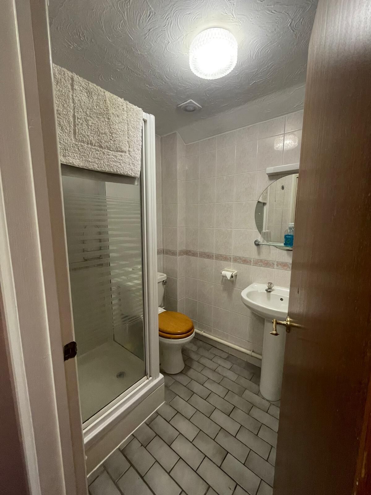 Un baño con mampara de vidrio, inodoro con asiento de madera, lavabo y espejo sobre él.