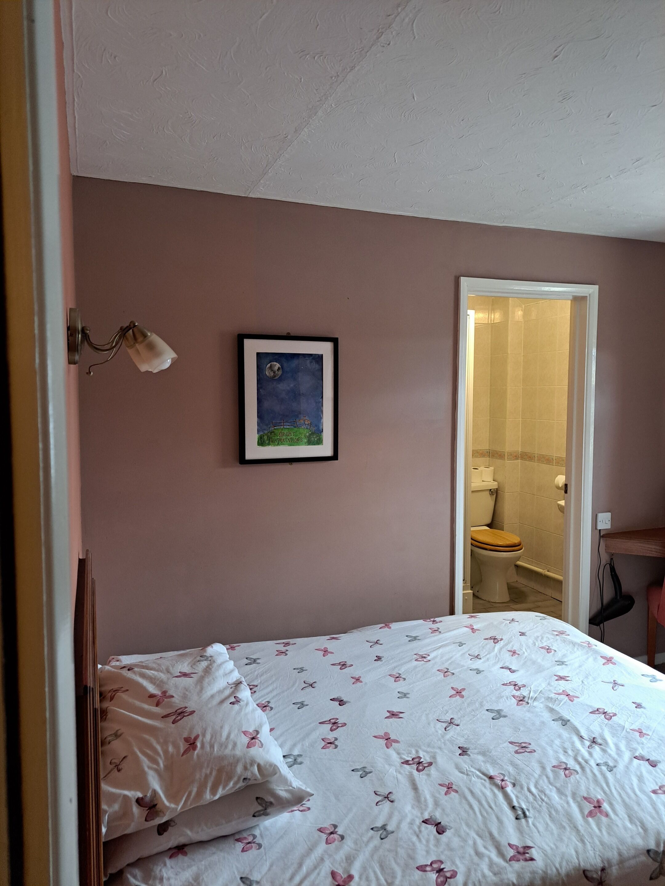 Un dormitorio con cama, un cuadro enmarcado en la pared y un baño visible a través de una puerta abierta.