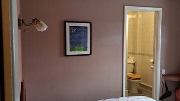 Un dormitorio con cama, un cuadro enmarcado en la pared y un baño visible a través de una puerta abierta.