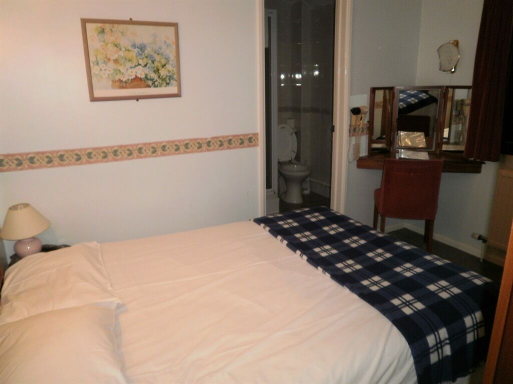 A bedroom with a bed, a nightstand, a lamp, a bathroom door, and a mirror.