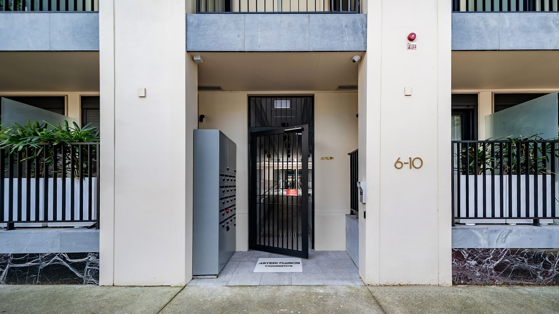 A building entrance with a metal gate, a fire alarm, and a mailbox.