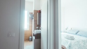 Moderni hotellihuone, jossa on puulattia, suuri sänky, jossa on kukallinen päiväpeite, yöpöytä sekä kylpyhuone, jossa on pesuallas ja peili.