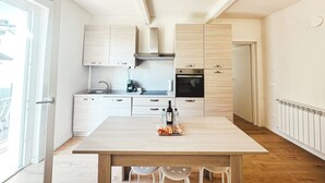 Moderni keittiö, jossa on puiset kaapit, sisäänrakennettu uuni ja ruokapöytä tuoleineen.