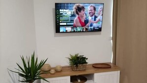 A flat-screen TV mounted on a wall above a wooden console with shelves and decorative items. - Estudio Nuevo con Jardín Privado en Pleno Valle (La Laguna)