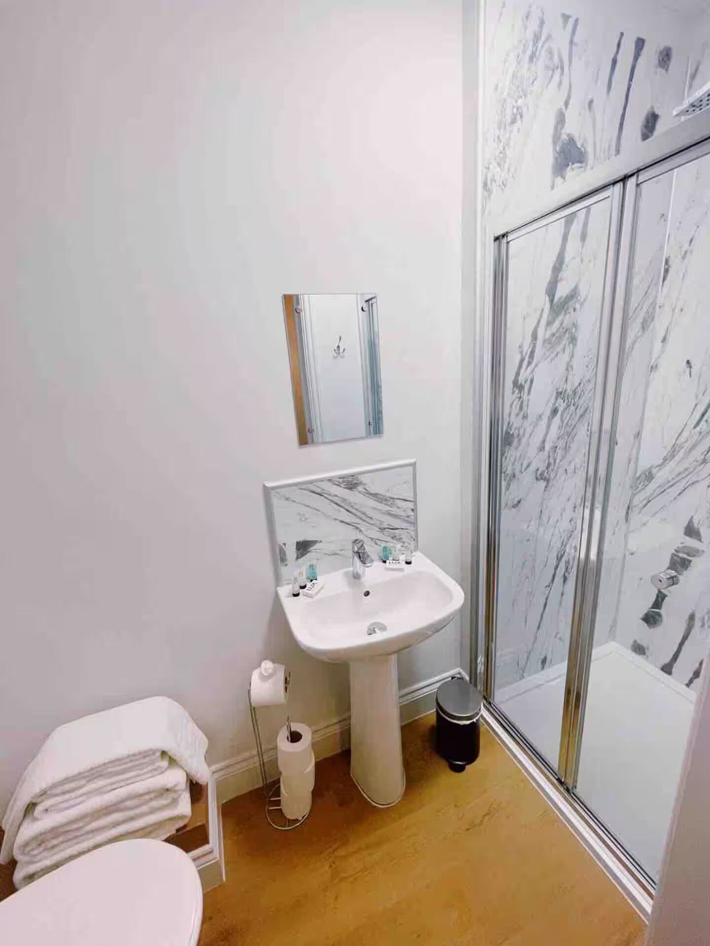 Ein Badezimmer mit weißem Waschbecken, einem Spiegel, einer Toilette und einer Duschkabine.