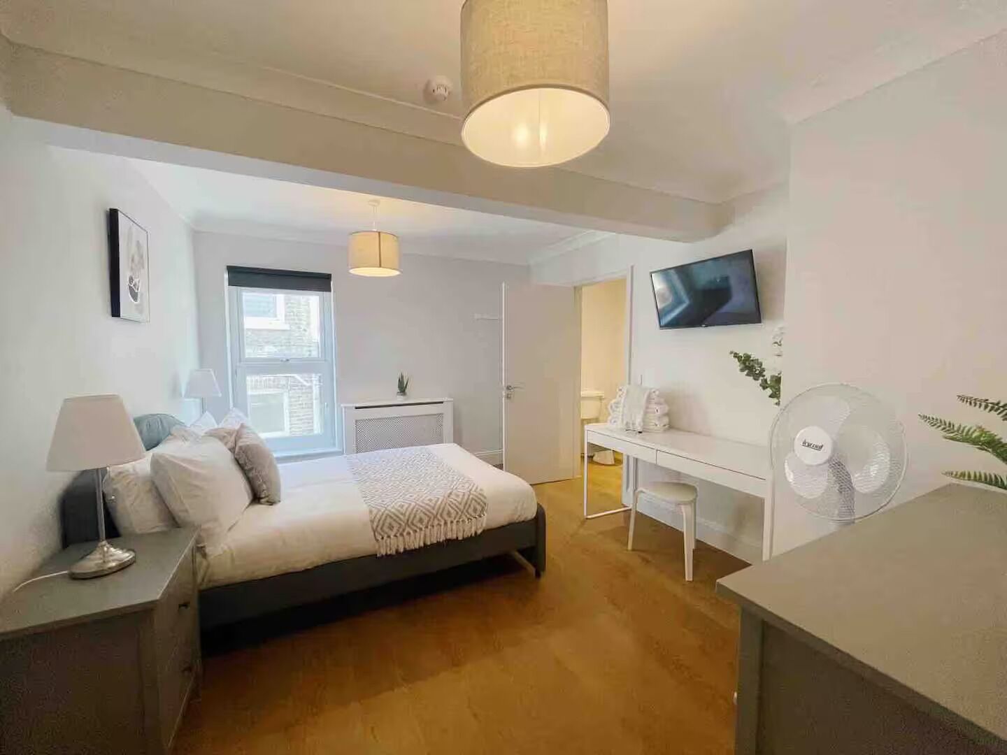 Ein modernes Schlafzimmer mit Bett, Nachttisch, Lampe und einem Fernseher an der Wand.