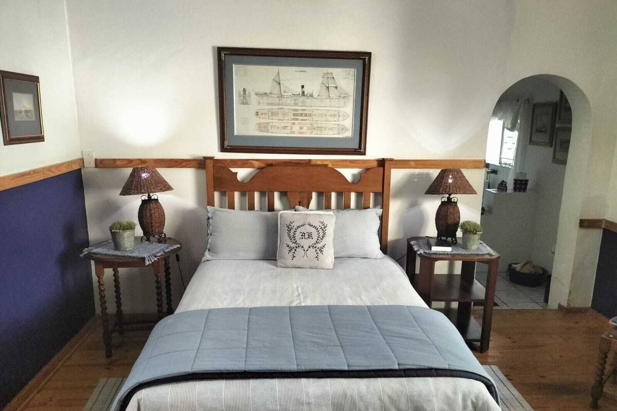 Une chambre à coucher bien aménagée, avec un grand lit, deux tables de chevet dotées de lampes, un tableau encadré au mur et une porte en arc donnant sur une autre pièce.