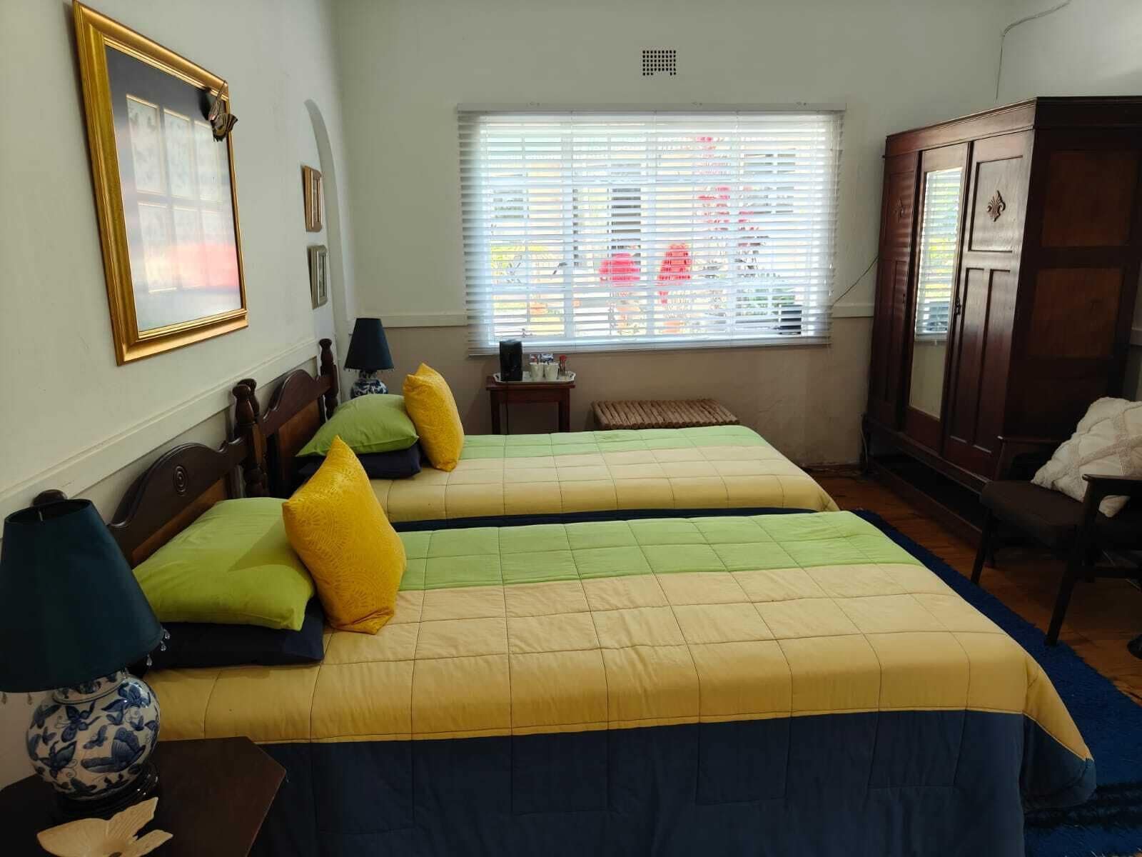 Habitación con dos camas, ventana con persianas, armario de madera y lámpara sobre una mesita de noche.