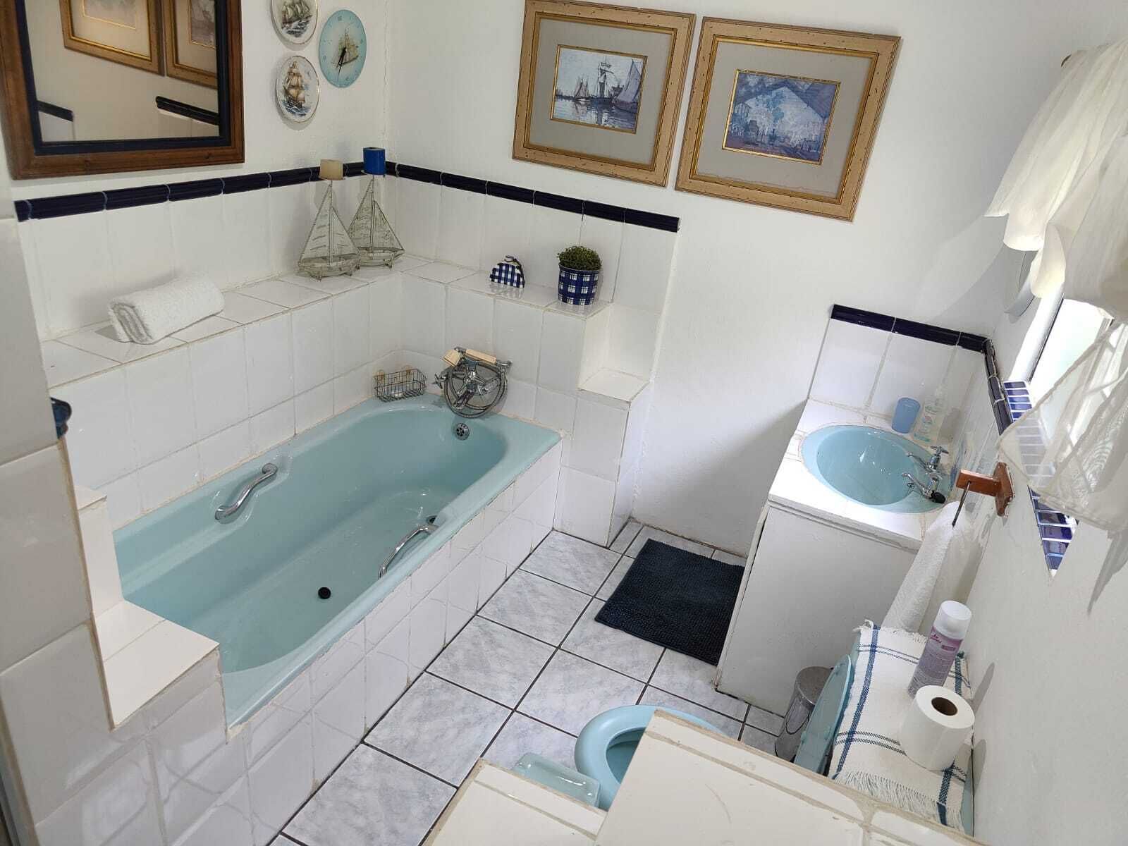 A bathroom with a bathtub, toilet, sink, and decorative items like framed pictures and a small shelf.