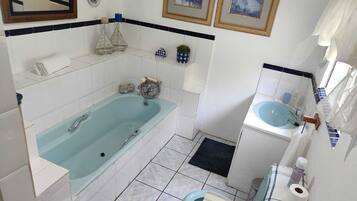 A bathroom with a bathtub, toilet, sink, and decorative items like framed pictures and a small shelf.