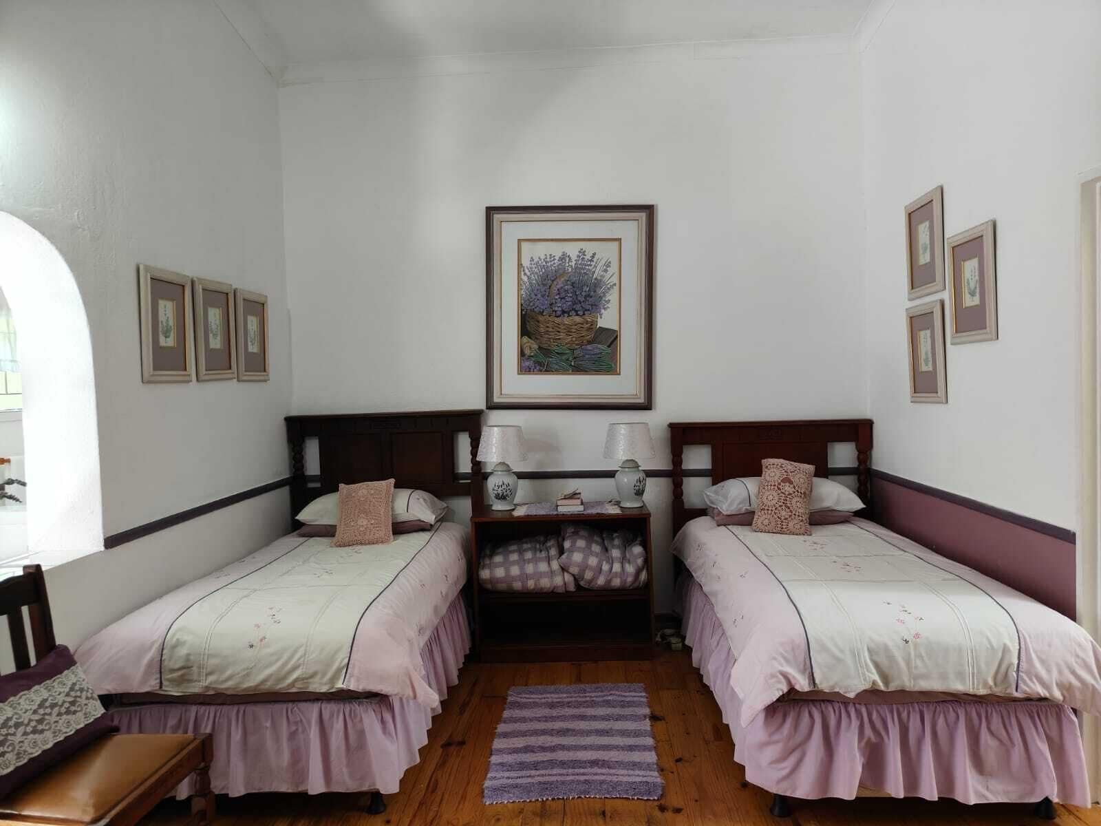 A room with two beds, a wooden bench, a small table, and a framed picture on the wall.