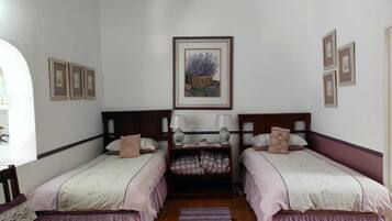 A room with two beds, a wooden bench, a small table, and a framed picture on the wall.