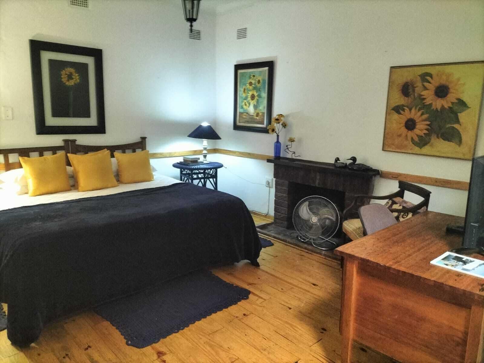 A bedroom with a bed, bedside table, lamp, fireplace, and artwork.