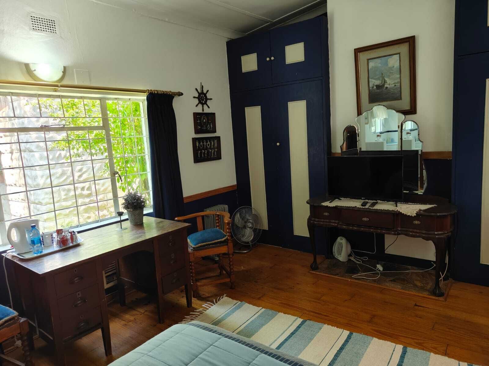 A room with a wooden desk, a chair, a radiator, a fan, and a piano.