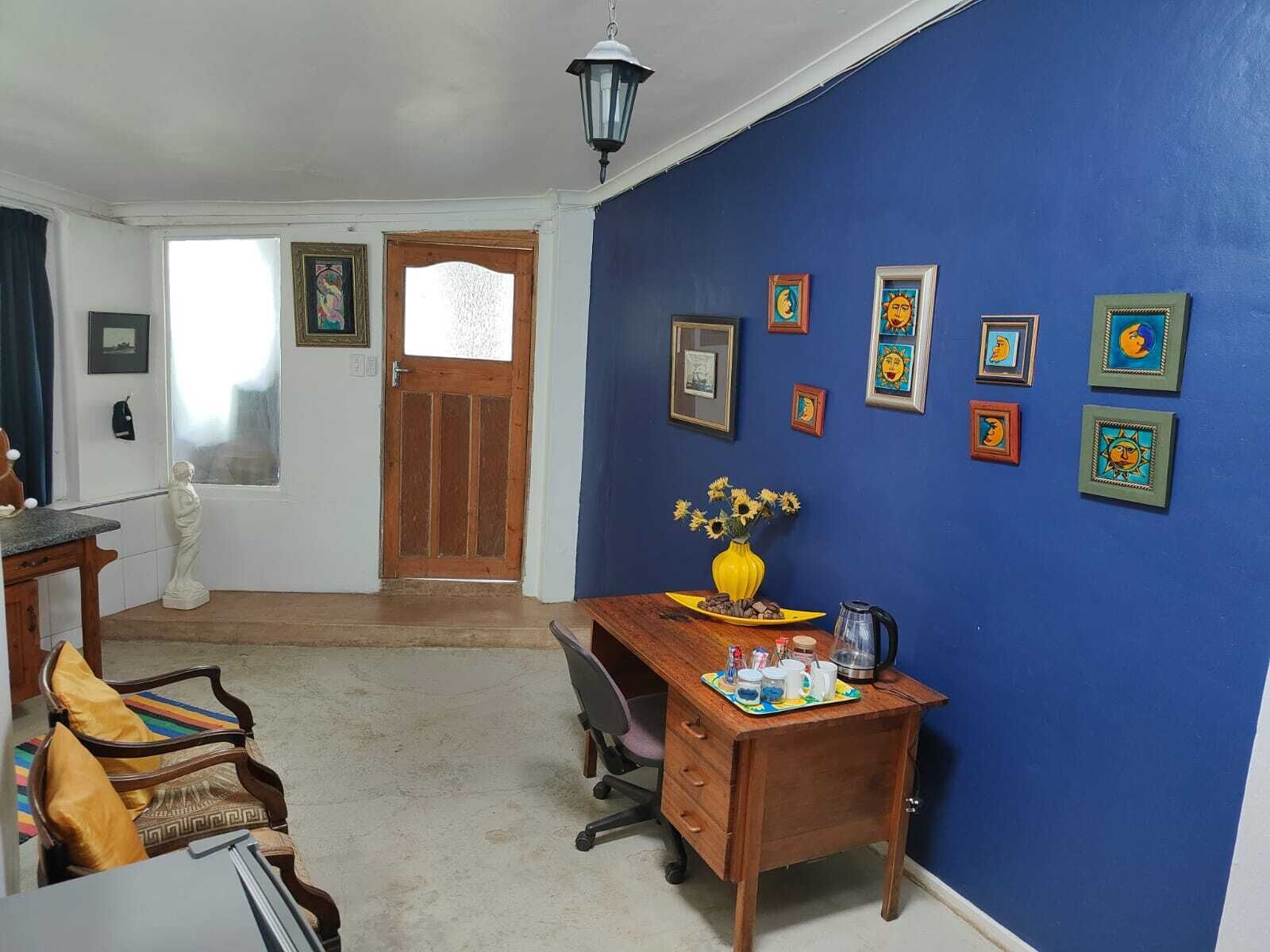 Una habitación con un escritorio de madera, una silla, un jarrón con flores y un cuadro con marcos.