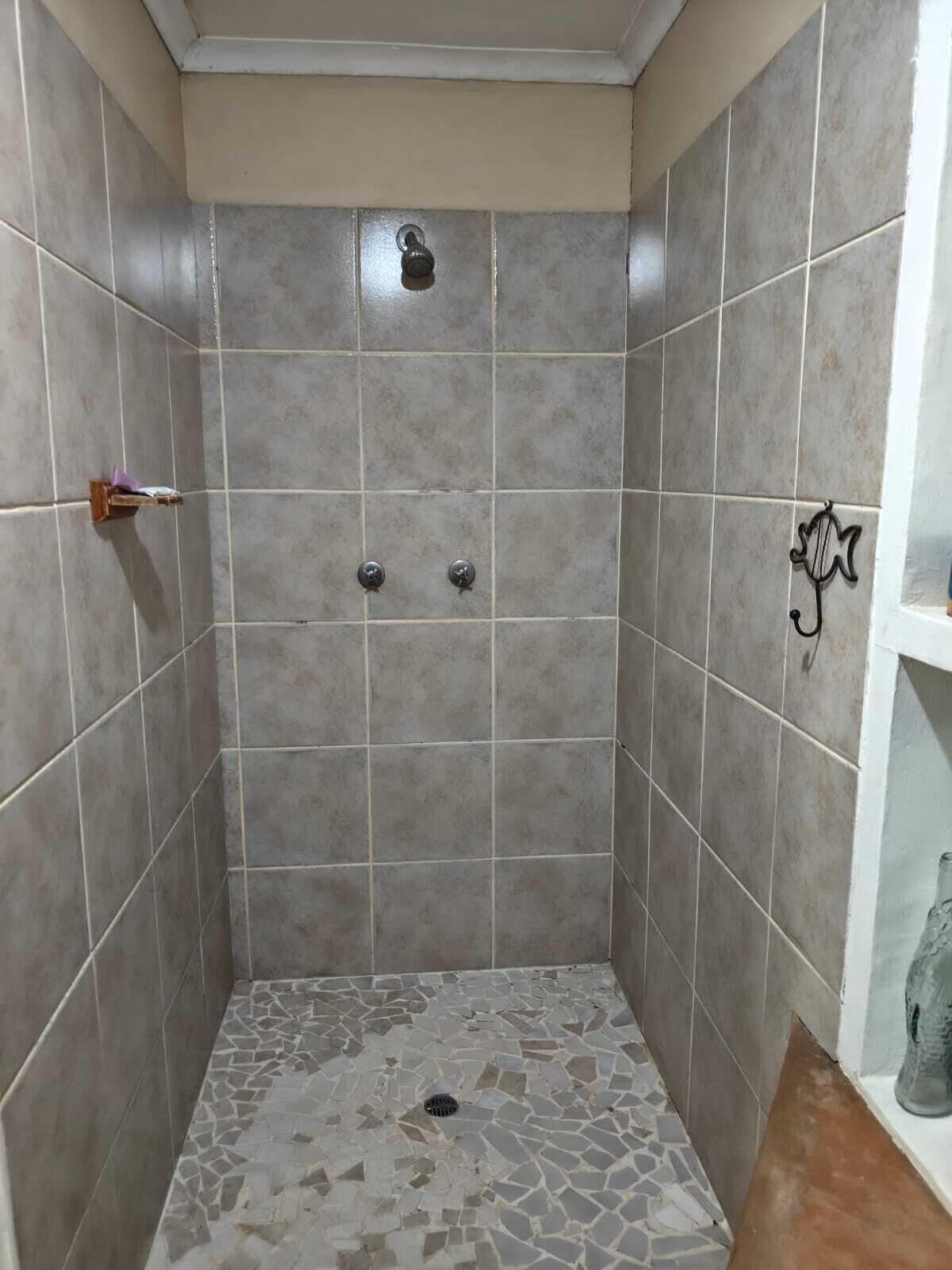 A small, tiled shower room with a drain in the center, a shelf with a bottle, and a towel rack on the wall.