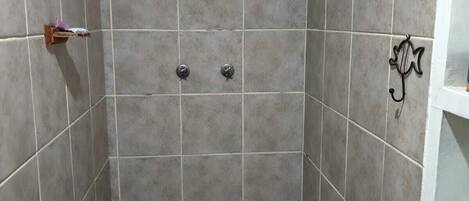 Un pequeño baño con azulejos, un desagüe central, un estante con una botella y un perchero en la pared.