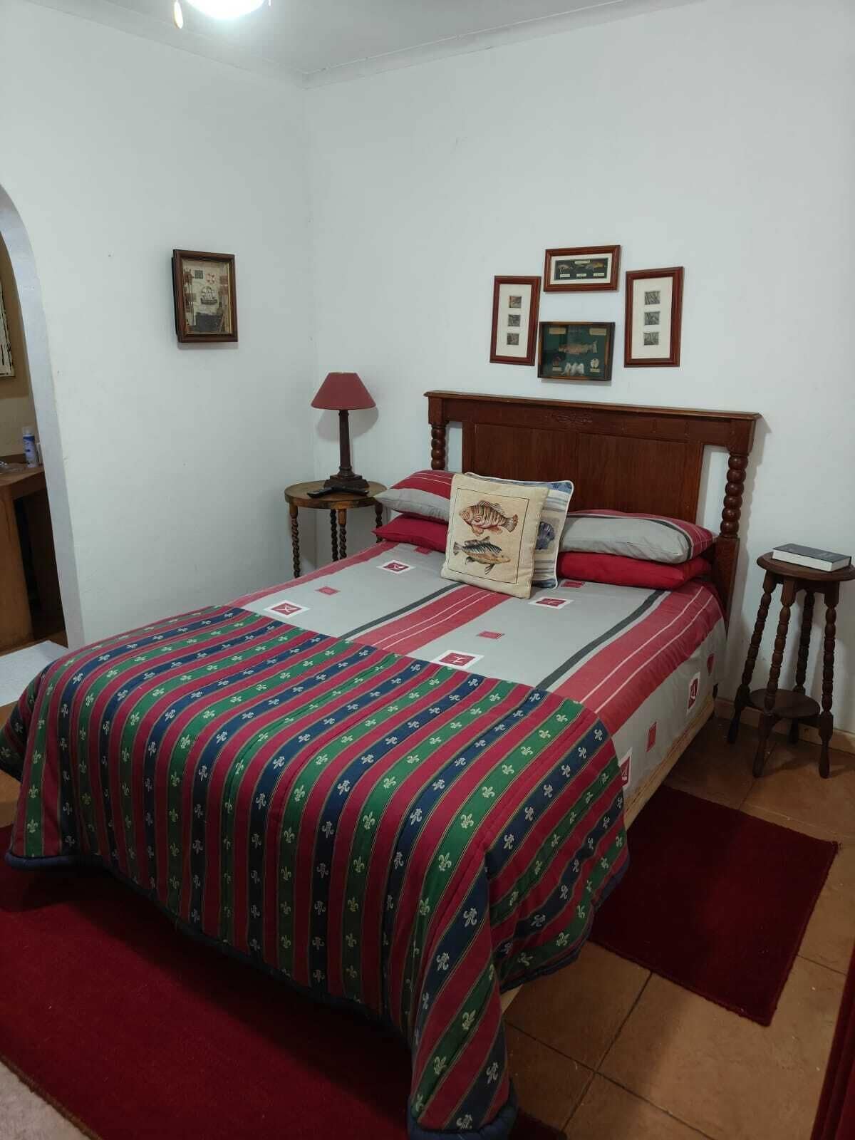 Un dormitorio con cama, mesita de noche, lámpara y cuadros en la pared.