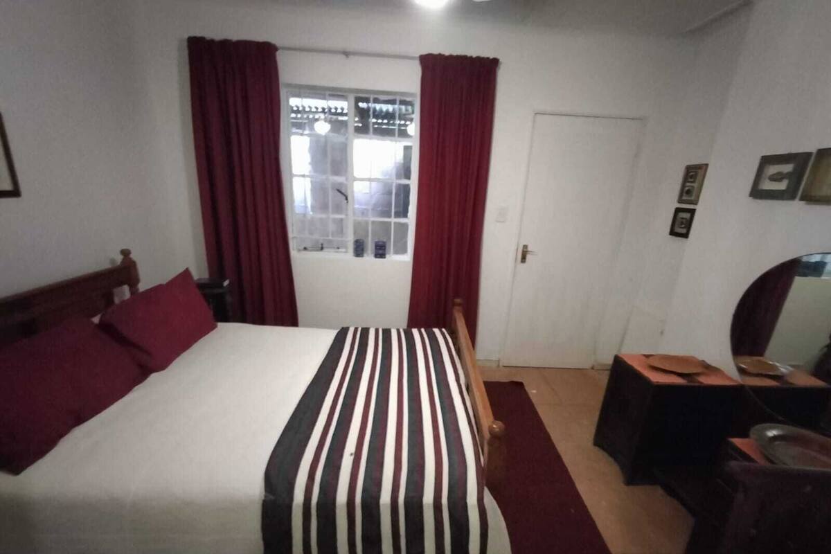 Une chambre à coucher avec un lit, un bureau, une chaise, une fenêtre avec des rideaux et une porte.