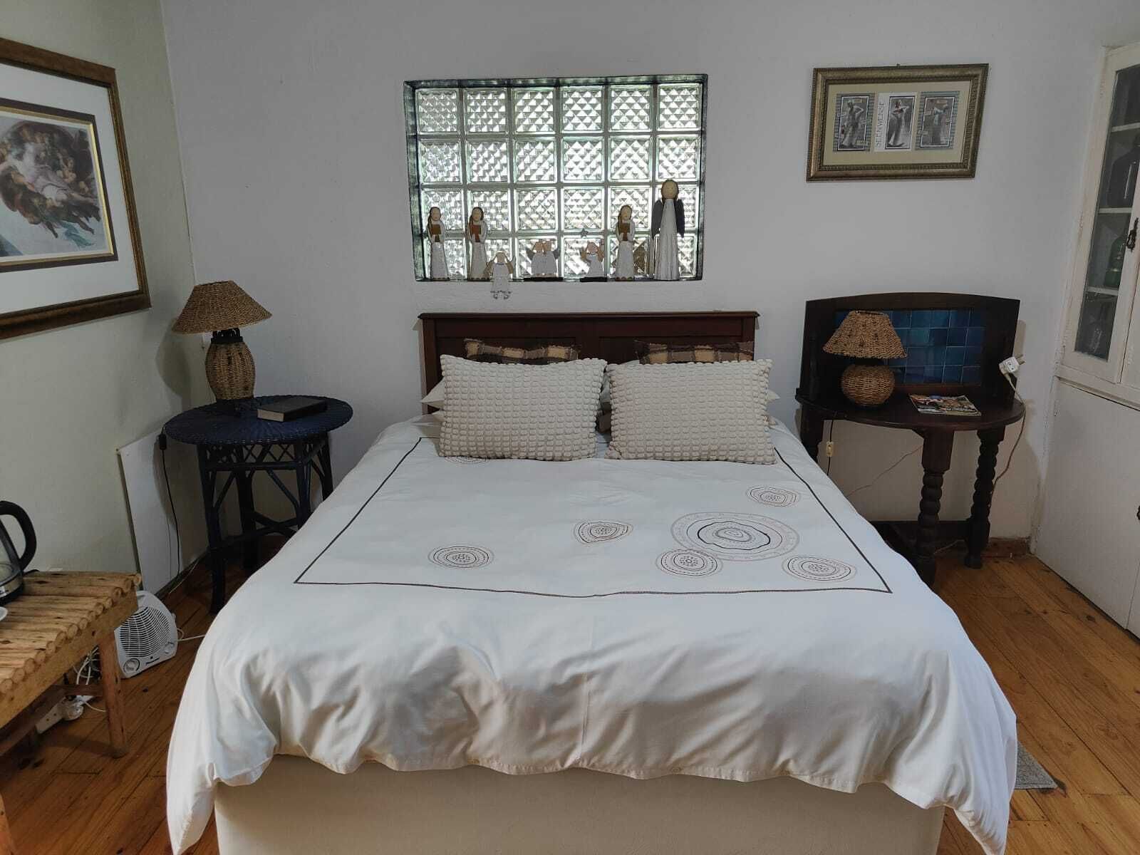 Un dormitorio con una cama grande, una ventana con diseño de celosía, una mesita redonda y una silla.