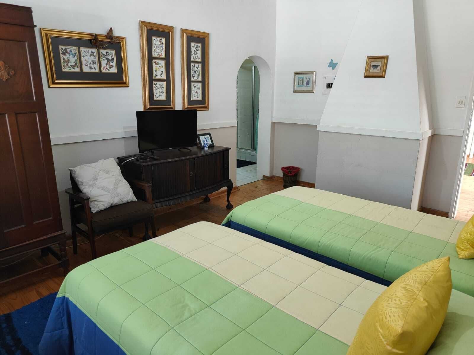 Une chambre avec deux lits, une commode en bois, un téléviseur et des œuvres d’art encadrées accrochées au mur.