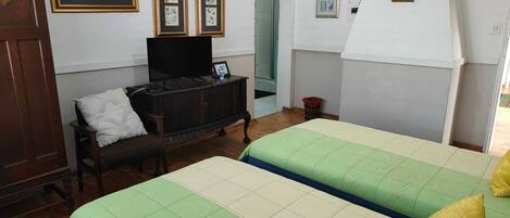 Une chambre avec deux lits, une commode en bois, un téléviseur et des œuvres d’art encadrées accrochées au mur.