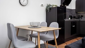 Une cuisine moderne avec un réfrigérateur noir, une machine à café et un four encastré. On y trouve une table à manger avec quatre chaises grises et une petite plante accrochée au mur.