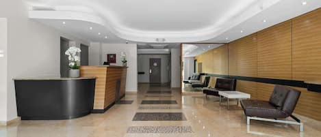 A modern reception area with a curved black reception desk, a wooden panel wall, and a seating area with leather chairs and a small table.