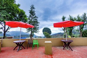 A terrace with two red umbrellas, a green chair, and a table with a view of mountains. - Hotel Shree Homestay (Ootacamund)