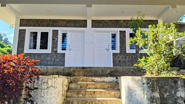 A two-story house with a stone facade, white doors, and a set of concrete stairs leading to the entrance. - Hotel Shree Homestay (Ootacamund)