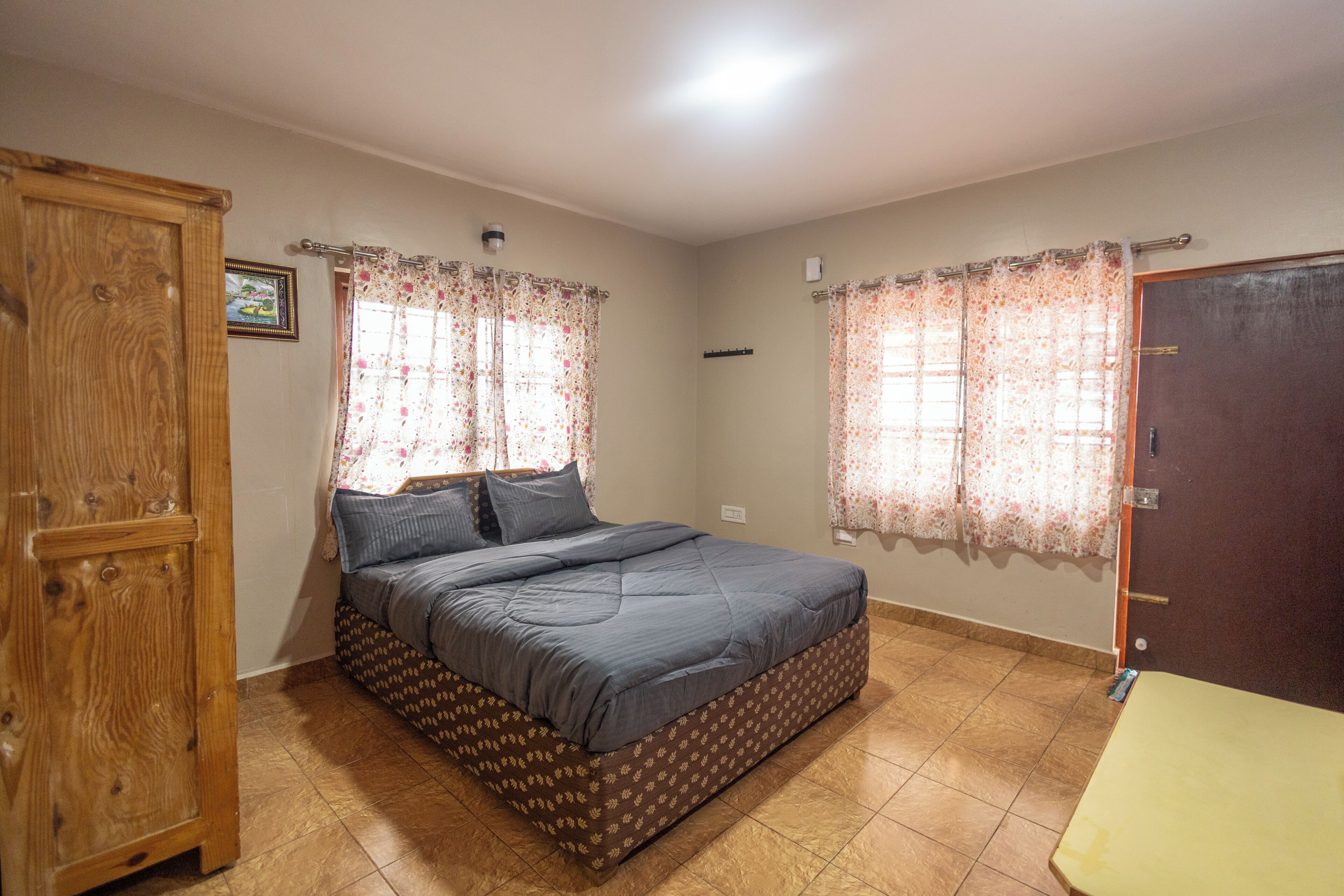 A bedroom with a bed, curtains, a wooden wardrobe, and a door.