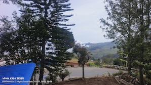 A rural road with trees and a hilly landscape in the background. - Hotel Shree Homestay (Ootacamund)