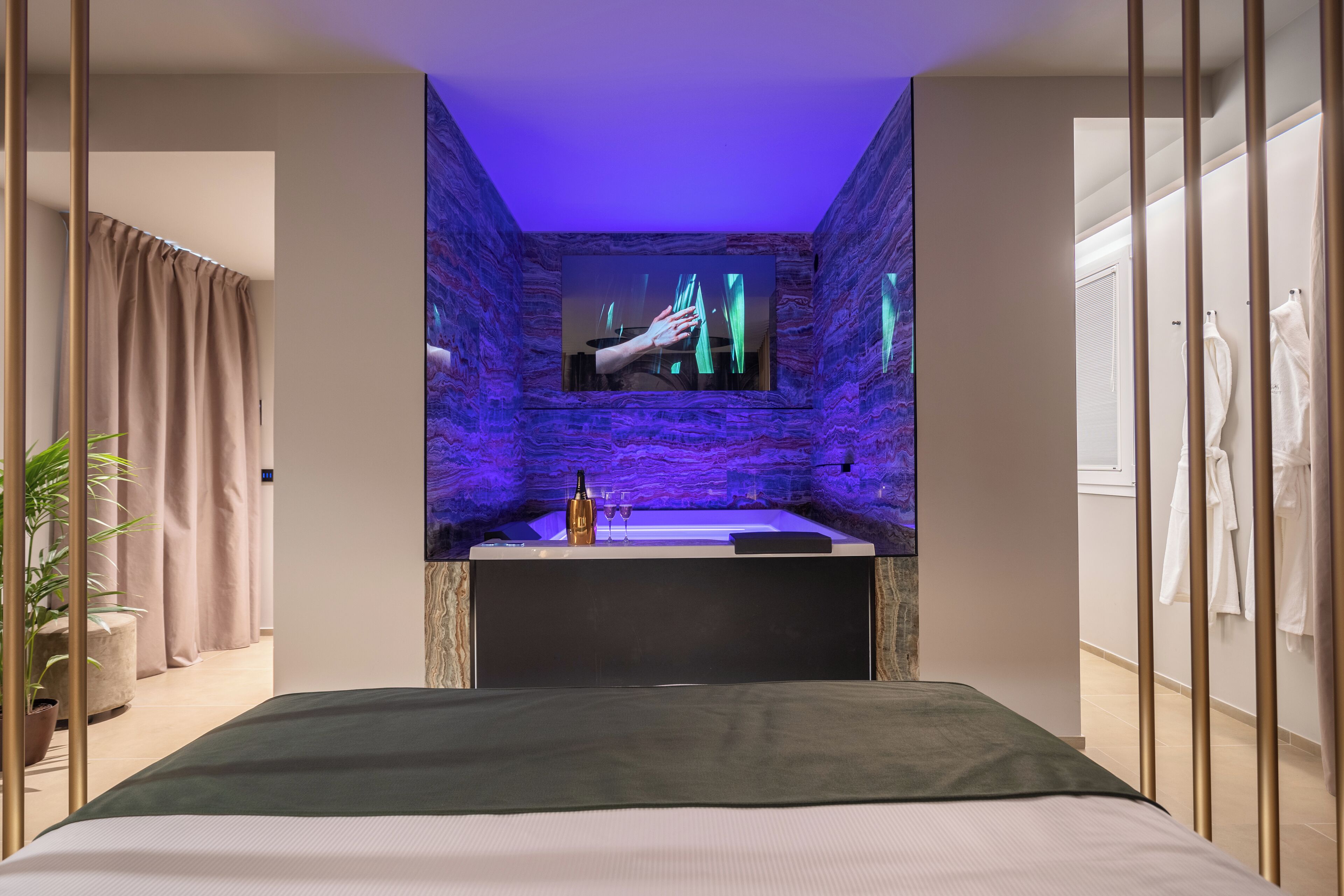 Una habitación de hotel moderna con una cama grande, televisión integrada, baño con bañera y una planta en maceta.