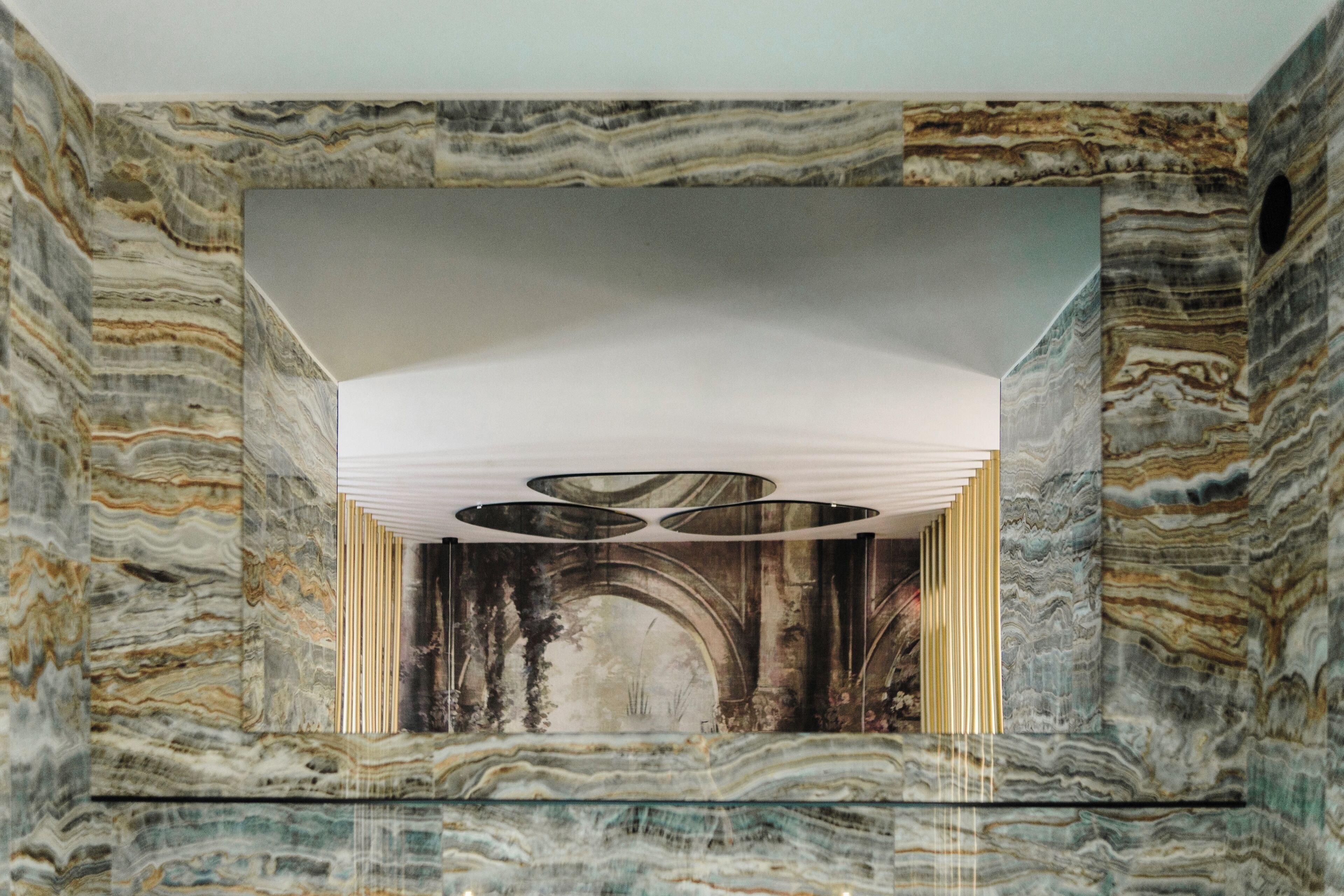 Un interno moderno con una parete in marmo, un arco centrale e un soffitto con lampade circolari.
