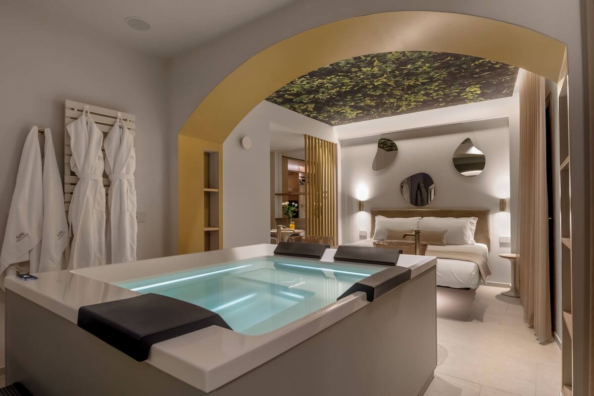 A modern hotel room with a spa tub, a bed, and a ceiling mural.