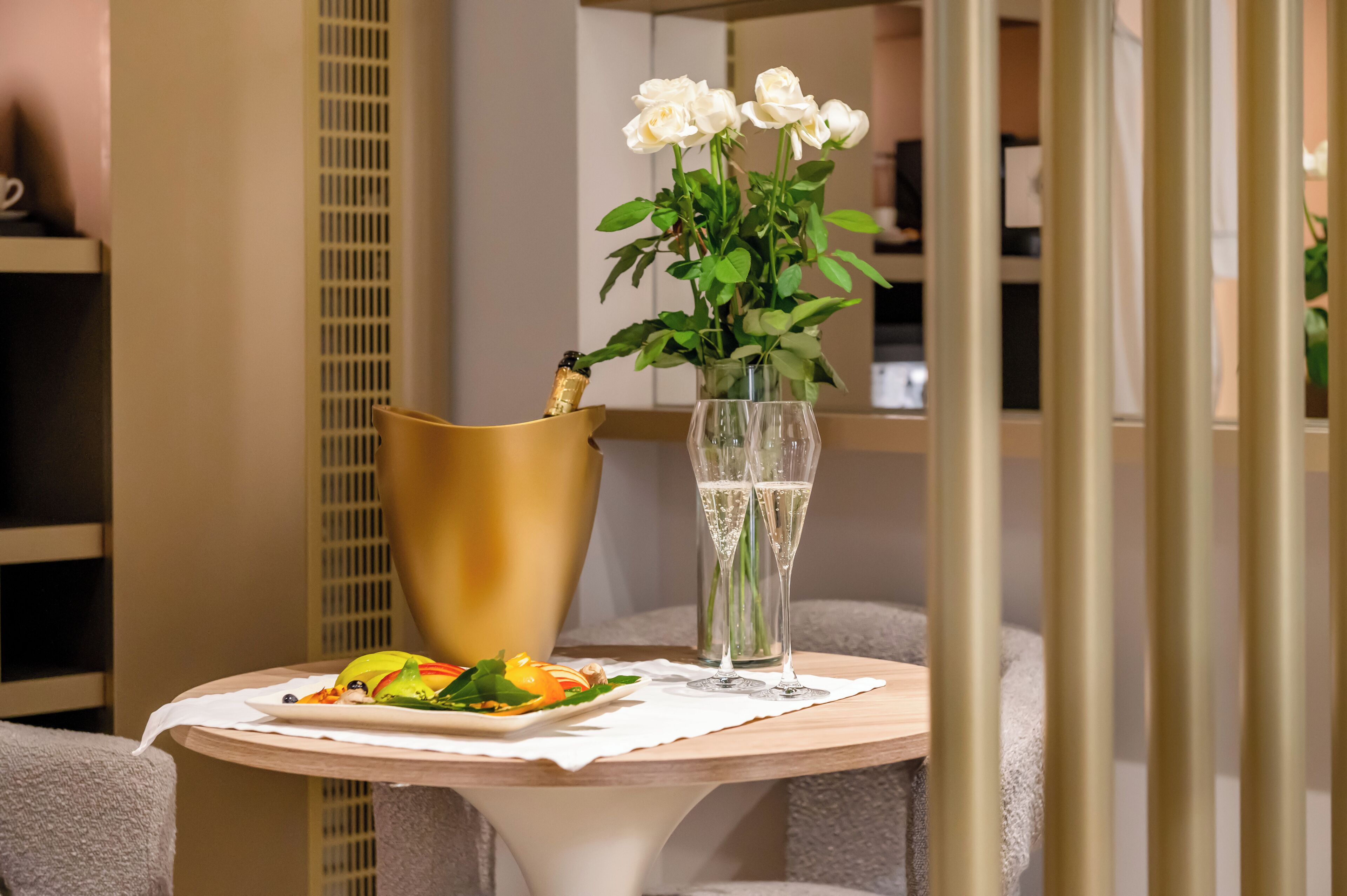 A table with a plate of food, a vase of white flowers, a champagne bottle, and two glasses of champagne.